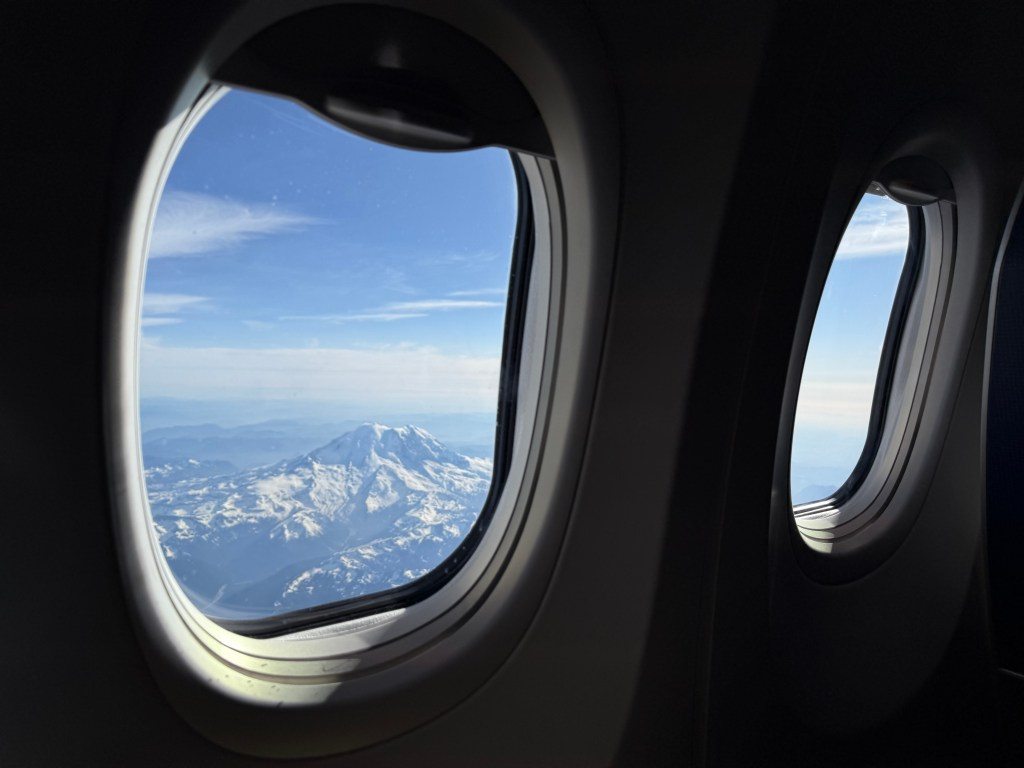 View of snow-capped mountains from an airplane window during descent into Seattle.