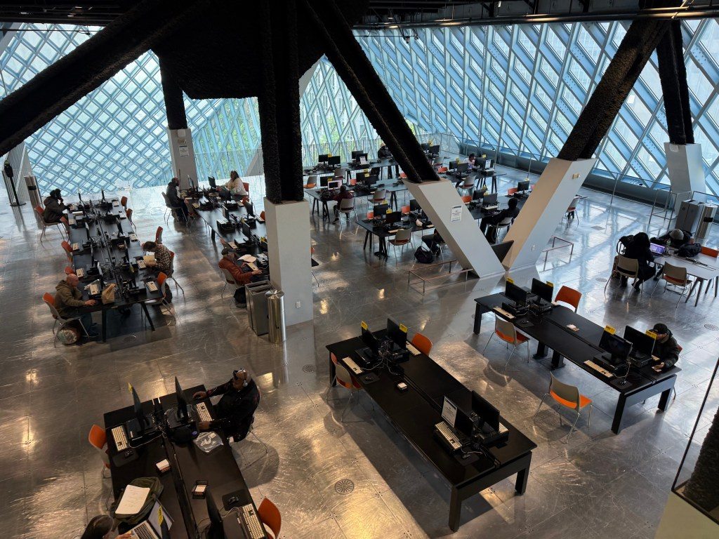 Interior view of Seattle Central Library, showcasing modern architecture and workstations with people using computers in a spacious environment.